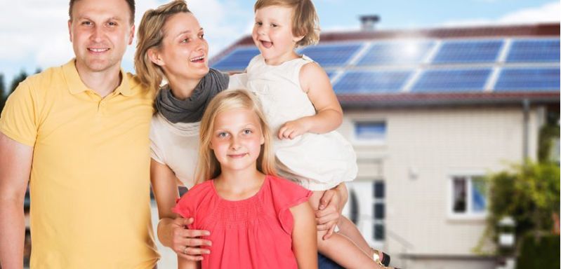 Happy Family Standing Together Outside The House With Solar Panel Fitted On Roof